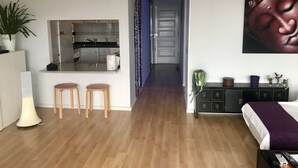 A modern hotel room with a kitchen area, a dining table with stools, a large bed with a purple blanket, and a wall-mounted artwork. - Central and large apartment with sea views (Las Palmas de Gran Canaria)