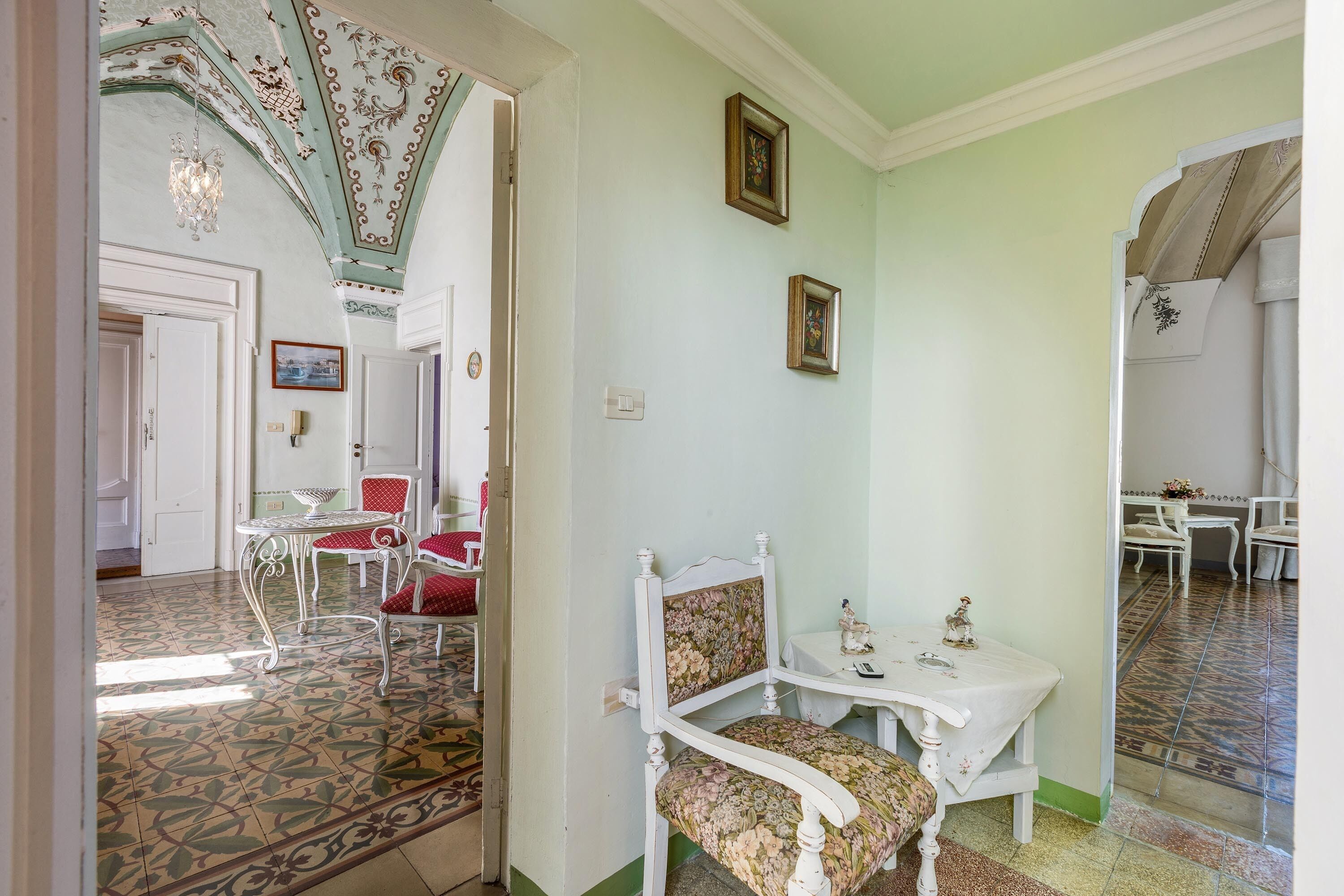 A room with a patterned floor, a white chair with floral upholstery, and a small table with a decorative item.