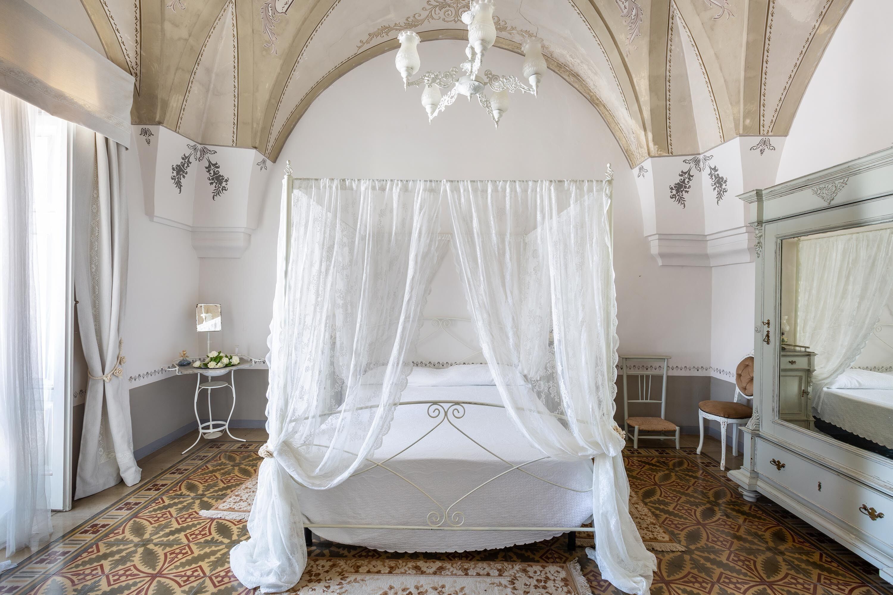 Un lit à baldaquin à quatre poteaux, surmonté d’un ciel de lit blanc, d’un lustre et d’un miroir.