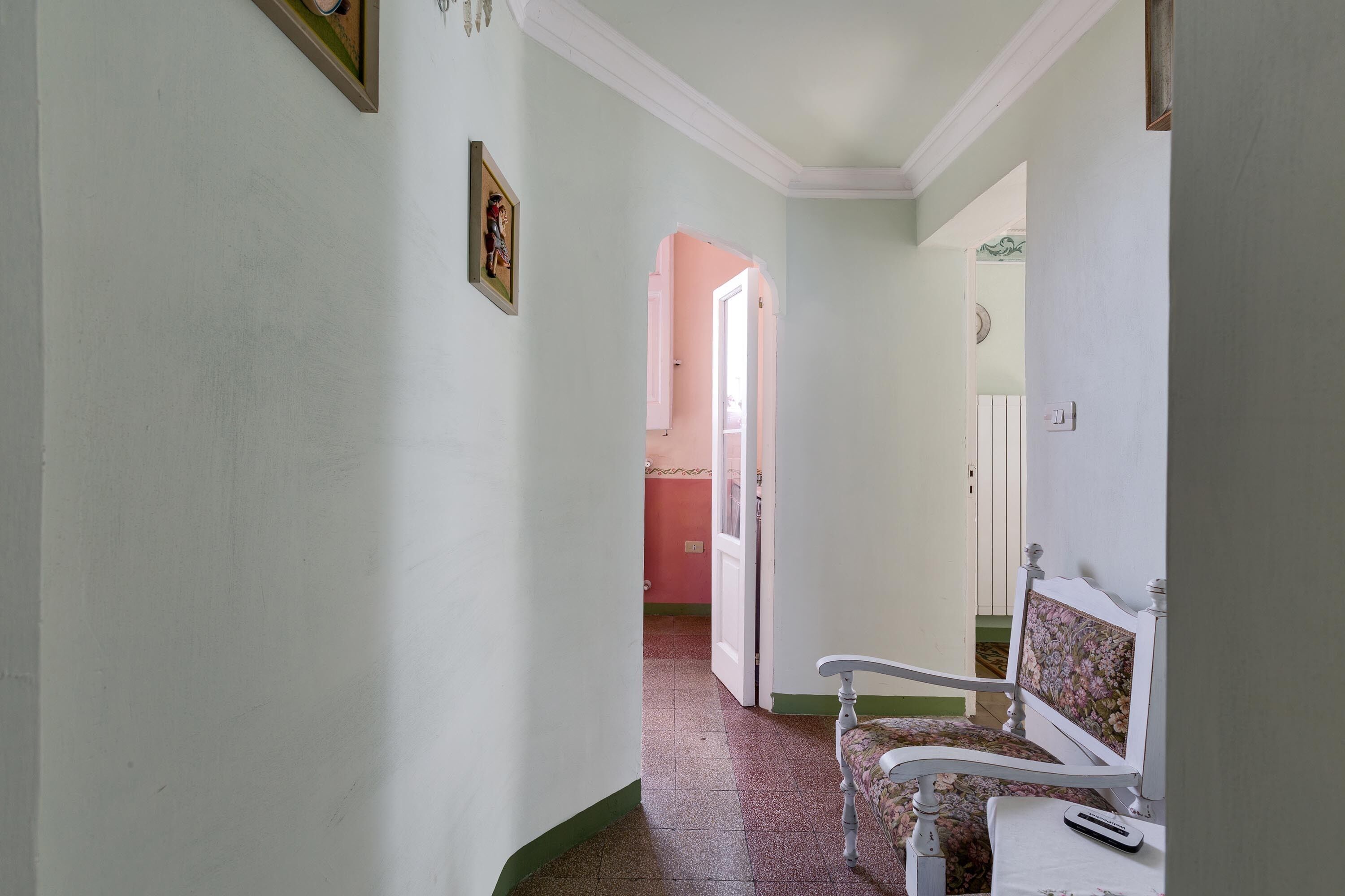 A hallway with a white chair and a table, a door leading to another room, and a framed picture on the wall.