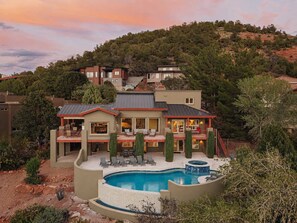 A large house with a swimming pool, multiple decks, and a view of a hilly landscape.