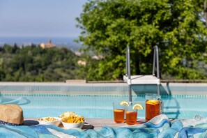 A poolside setting with a table, bowls of chips, glasses of tea, and a view of the sea and trees. - La Nocciola - Villa with private pool in Montefiore Conca, Emilia-Romagna (Montefiore Conca)