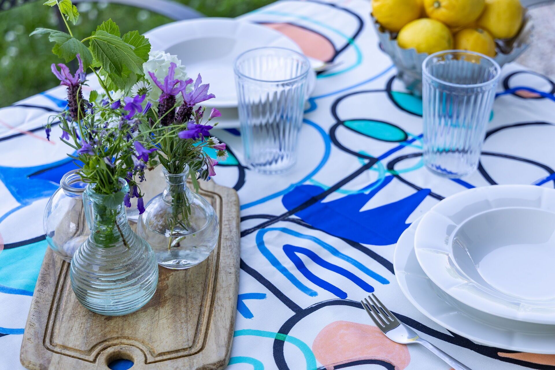 Una mesa dispuesta con jarrones de vidrio transparente con flores, un cuenco de limones y un plato blanco con un tenedor.