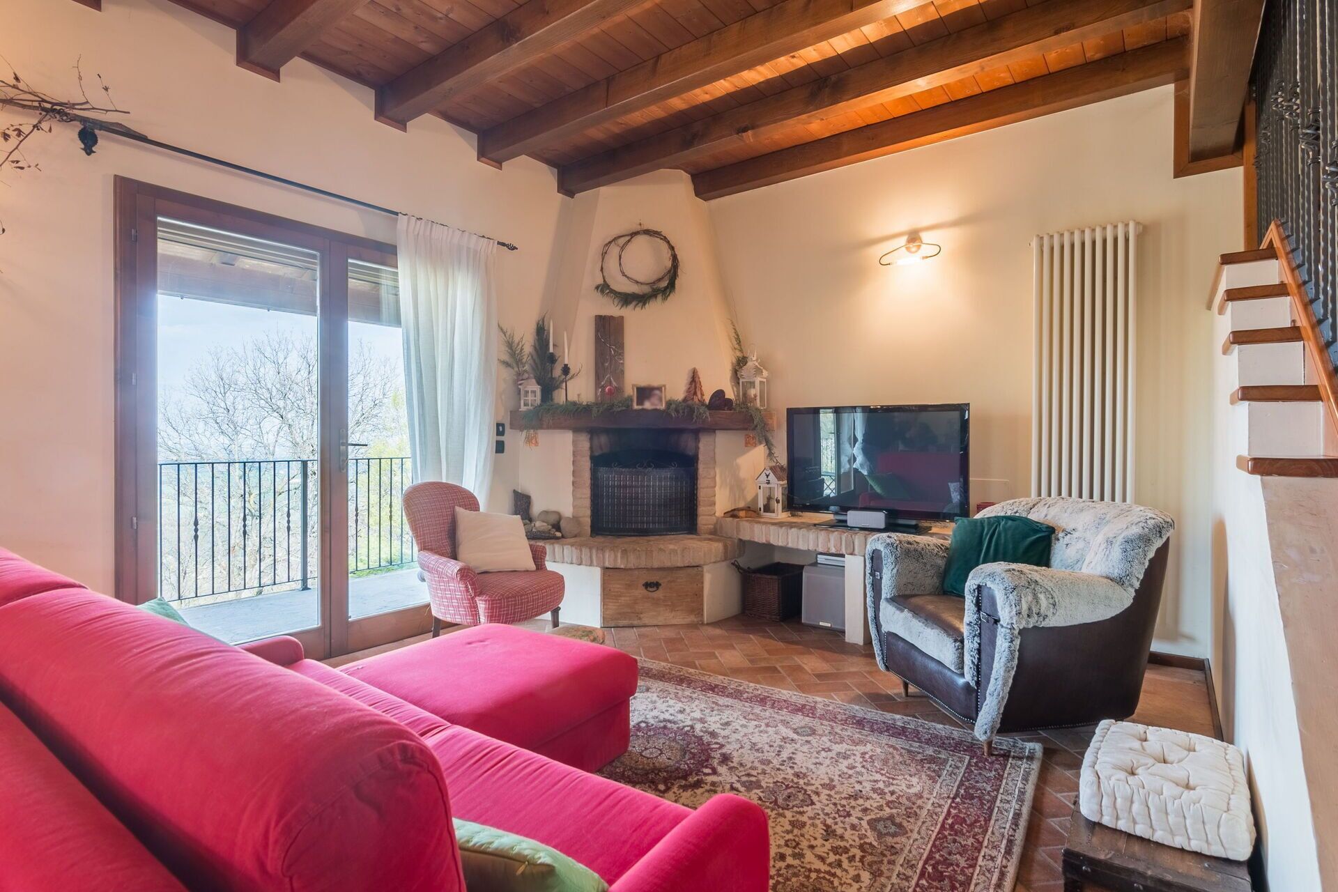 A cozy living room with a fireplace, a television, and a balcony with a view of trees.