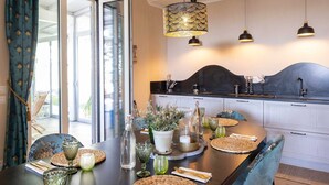 Una cocina moderna con comedor, que cuenta con un ventanal que da a un balcón, una encimera negra e iluminación colgante.