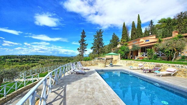 Una piscina con sillas de descanso, una terraza de piedra y vistas a un paisaje montañoso.