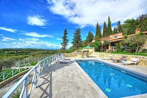Une piscine entourée de chaises longues, d’une terrasse en pierre et offrant une vue sur un paysage vallonné.