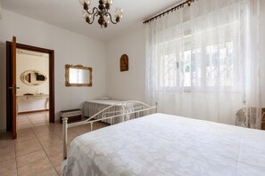 Ein Schlafzimmer mit Bett, Nachttisch, Spiegel und einem Fenster mit transparenten Vorhängen.