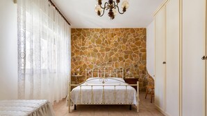 A bedroom with a stone-patterned wall, a bed with a metal frame, a chandelier, and a wooden nightstand. - 3266 Villetta Delle Viole by Barbarhouse (Torricella)