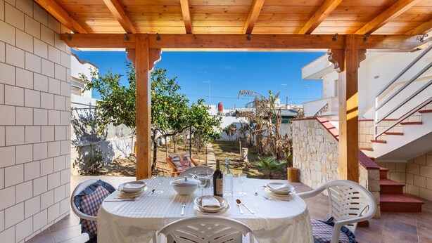 A covered outdoor dining area with a table set for four, surrounded by white chairs, under a wooden pergola. - 3266 Villetta Delle Viole by Barbarhouse (Torricella)