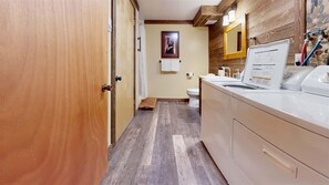 Un couloir étroit mène à une salle de bain dotée d’un plancher en bois, de toilettes blanches et d’un lavabo surmonté d’un miroir.