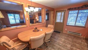 Un coin repas avec une table en bois et quatre chaises, un grand miroir et une fenêtre avec des stores.