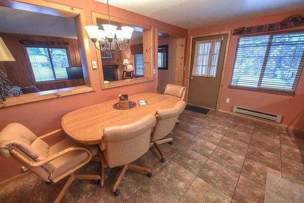 Un comedor con una mesa de madera y cuatro sillas, un espejo grande y una ventana con persianas.