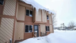 Un immeuble à plusieurs étages, dont le toit est recouvert de neige, et qui possède un porche à l’avant, avec une table et des chaises.