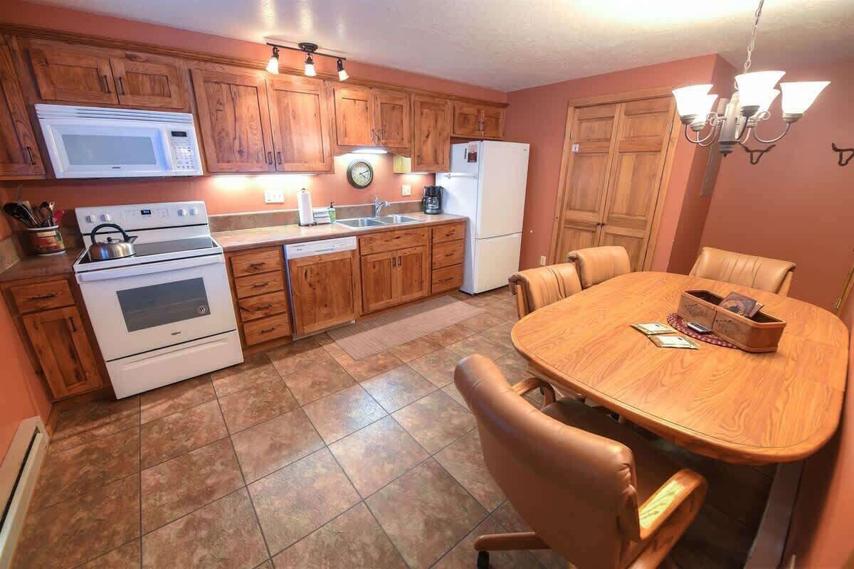 A kitchen with wooden cabinets, a microwave, stove, dishwasher, and a dining table with chairs.