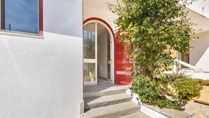 A staircase leading to a red door, a white wall, and a tree with green leaves. - 3268 Casa Doria by Barbarhouse (Alessano)
