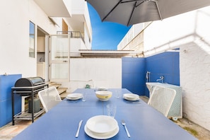Een eethoek met een blauwe tafel voor vier personen, een grill en uitzicht op de lucht.