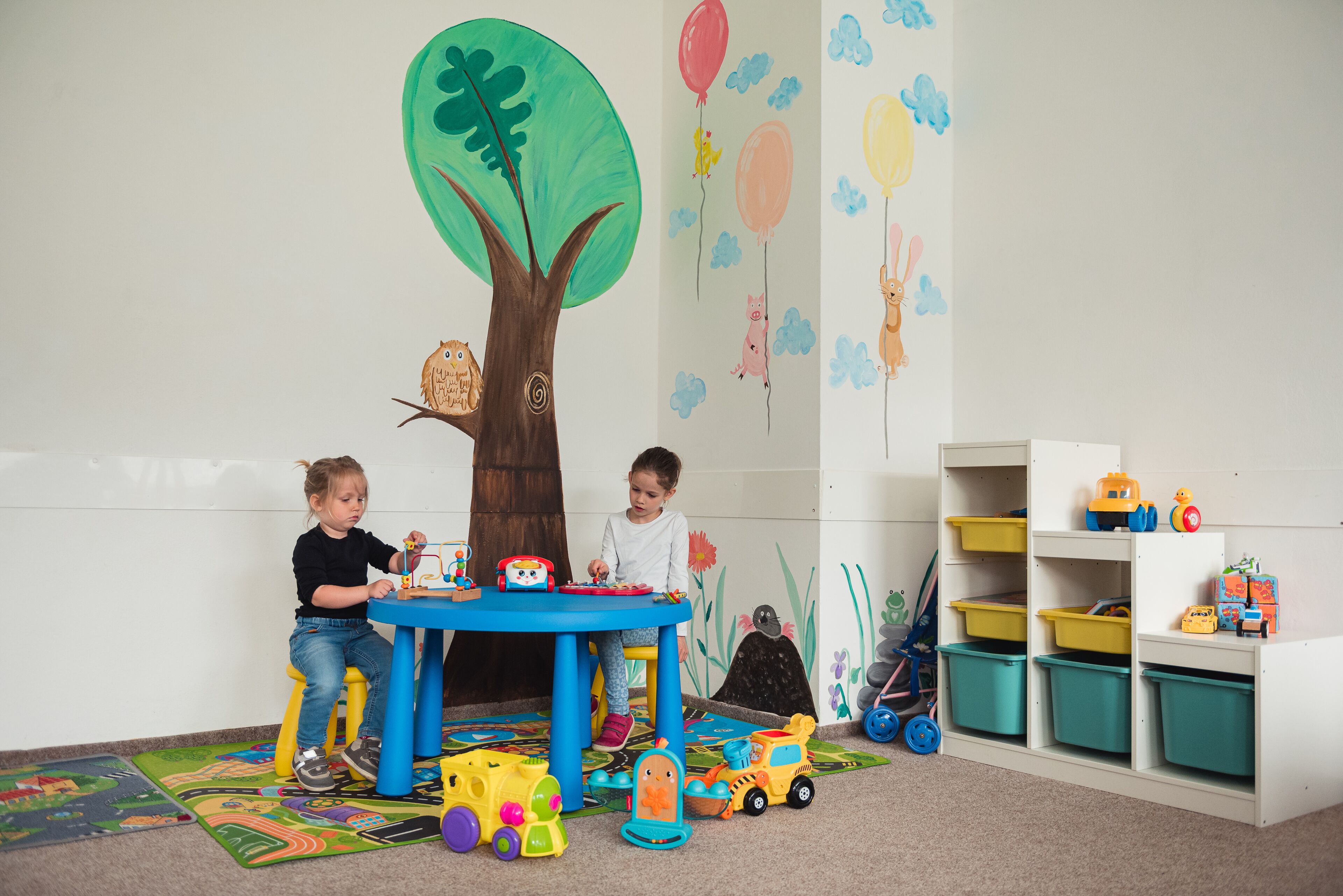 A playroom with a large tree mural, a table with toys, and storage bins.