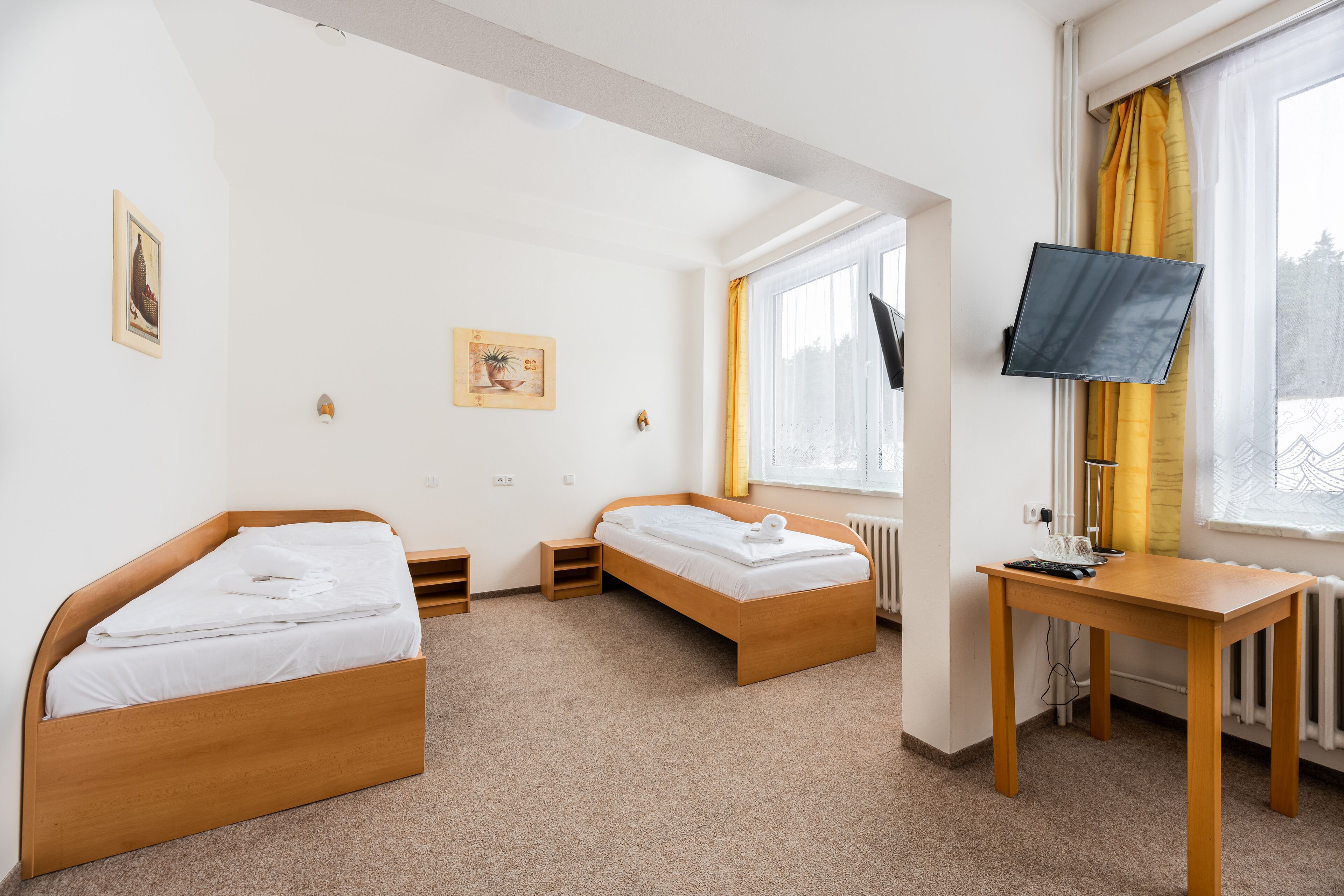 A room with two wooden beds, a desk, a television, and a window with curtains.