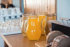 Una encimera de cocina con jarras de vidrio de jugo de naranja, una hogaza de pan y una tabla de cortar.
