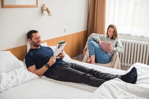 Un dormitorio con cama, almohadas, mesita de noche y ventana con cortinas.