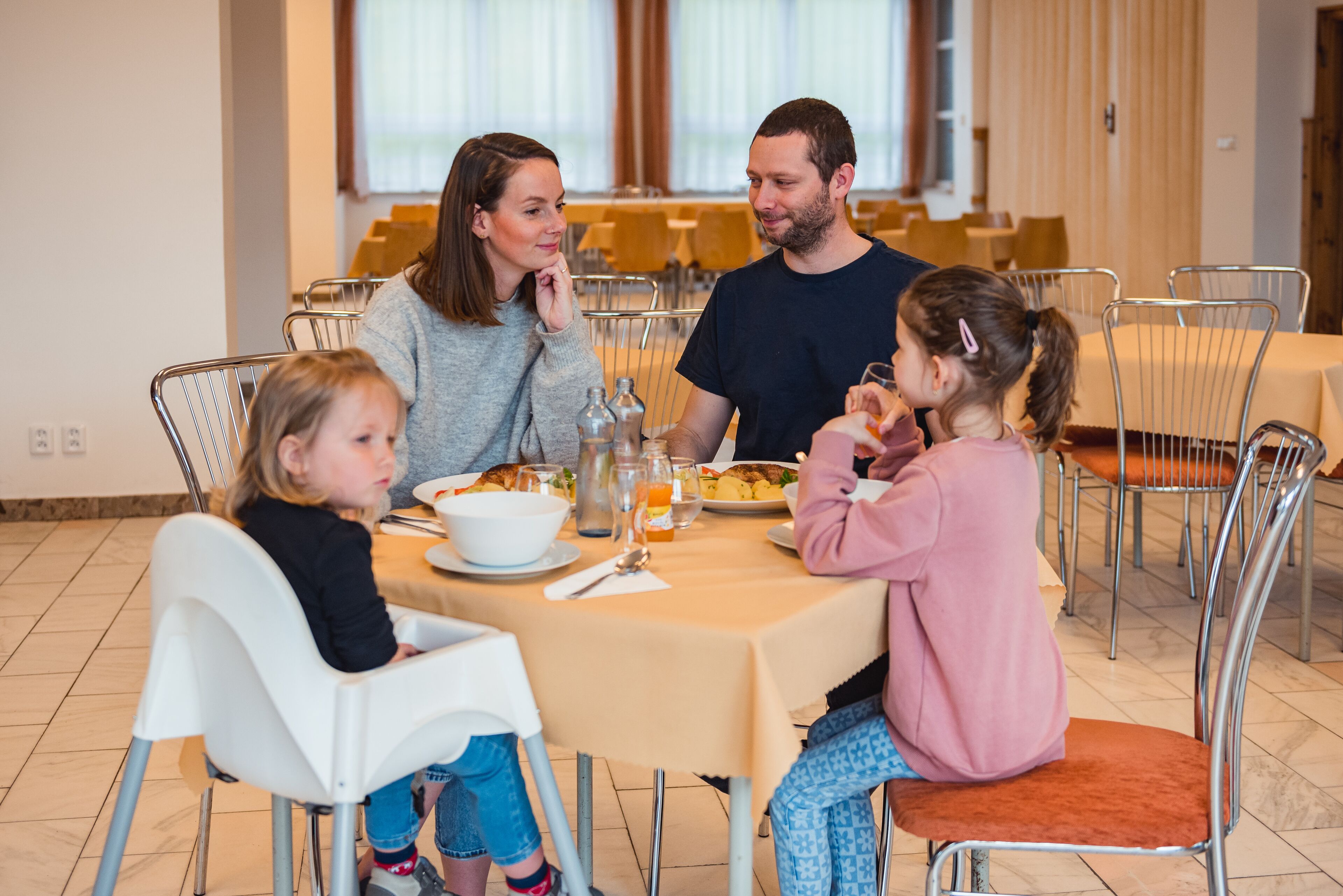 A family dining at a table with a beige tablecloth, surrounded by metal chairs.