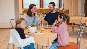 A family dining at a table with a beige tablecloth, surrounded by metal chairs.