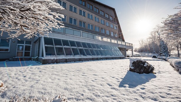 A building with a large glass facade, a snow-covered ground, and a clear sky. - HOTEL AGRI Soběšice (Sobešice)