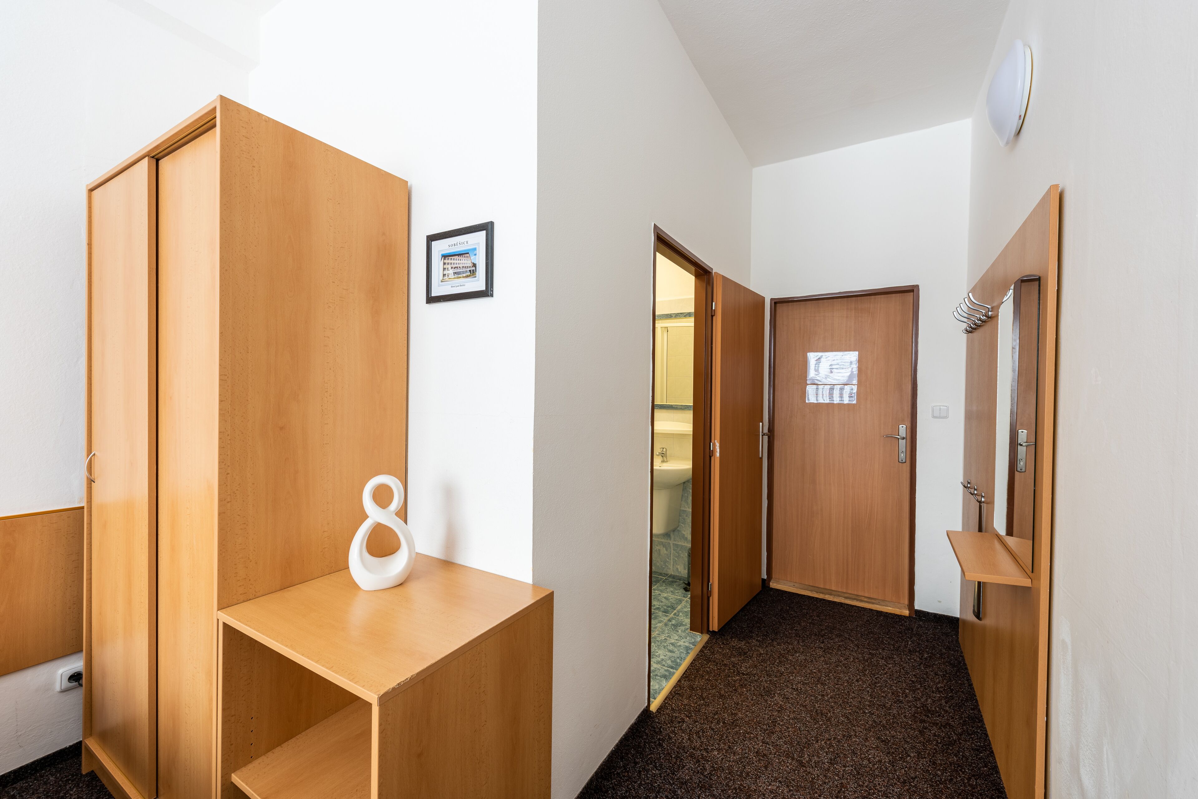 A hallway with wooden wardrobes, a small white shelf, and a framed certificate on the wall.