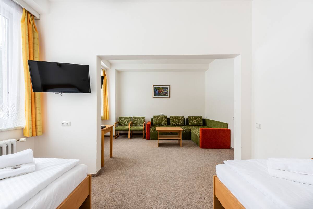 A hotel room with two single beds, a sofa, a small table, and a TV mounted on the wall.