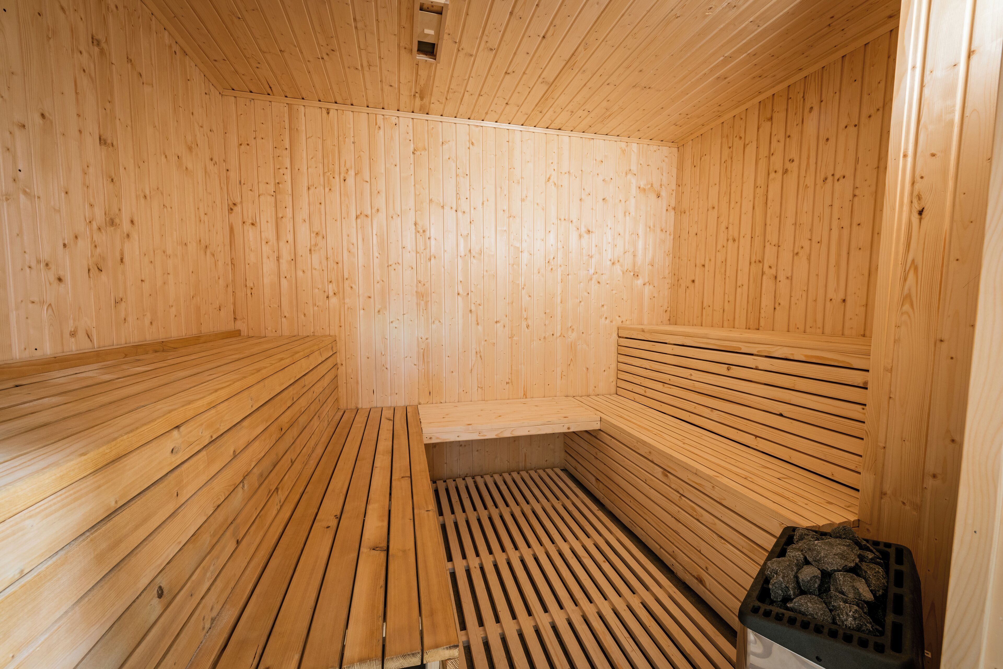 Una sauna con bancos de madera y un asiento tipo banca, suelo de madera y un cubo de basura negro.