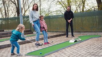 Um campo de mini golfe com superfície verde para tacadas, uma bola branca e alguns obstáculos.