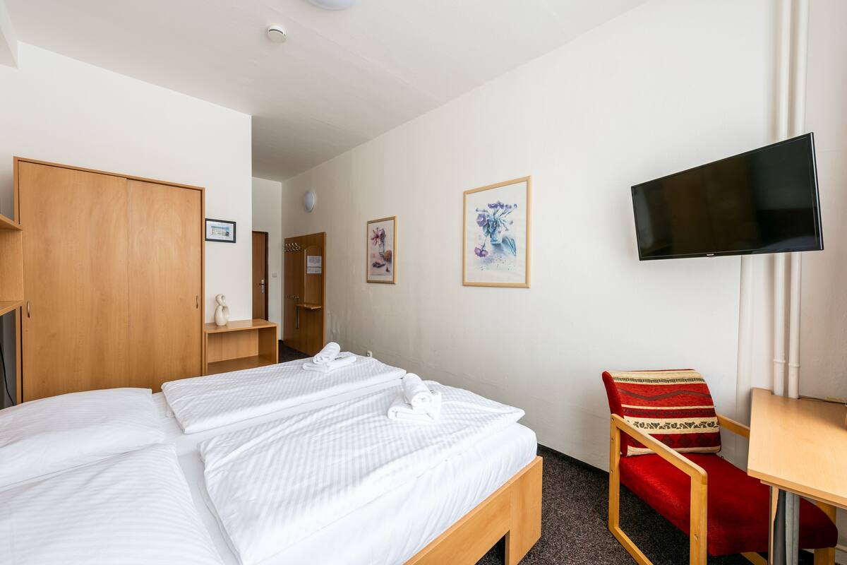 A hotel room with two beds, a TV, a chair, and a wooden wardrobe.