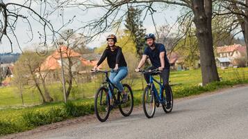 Två personer cyklar på en asfalterad stig, med träd och hus i bakgrunden.