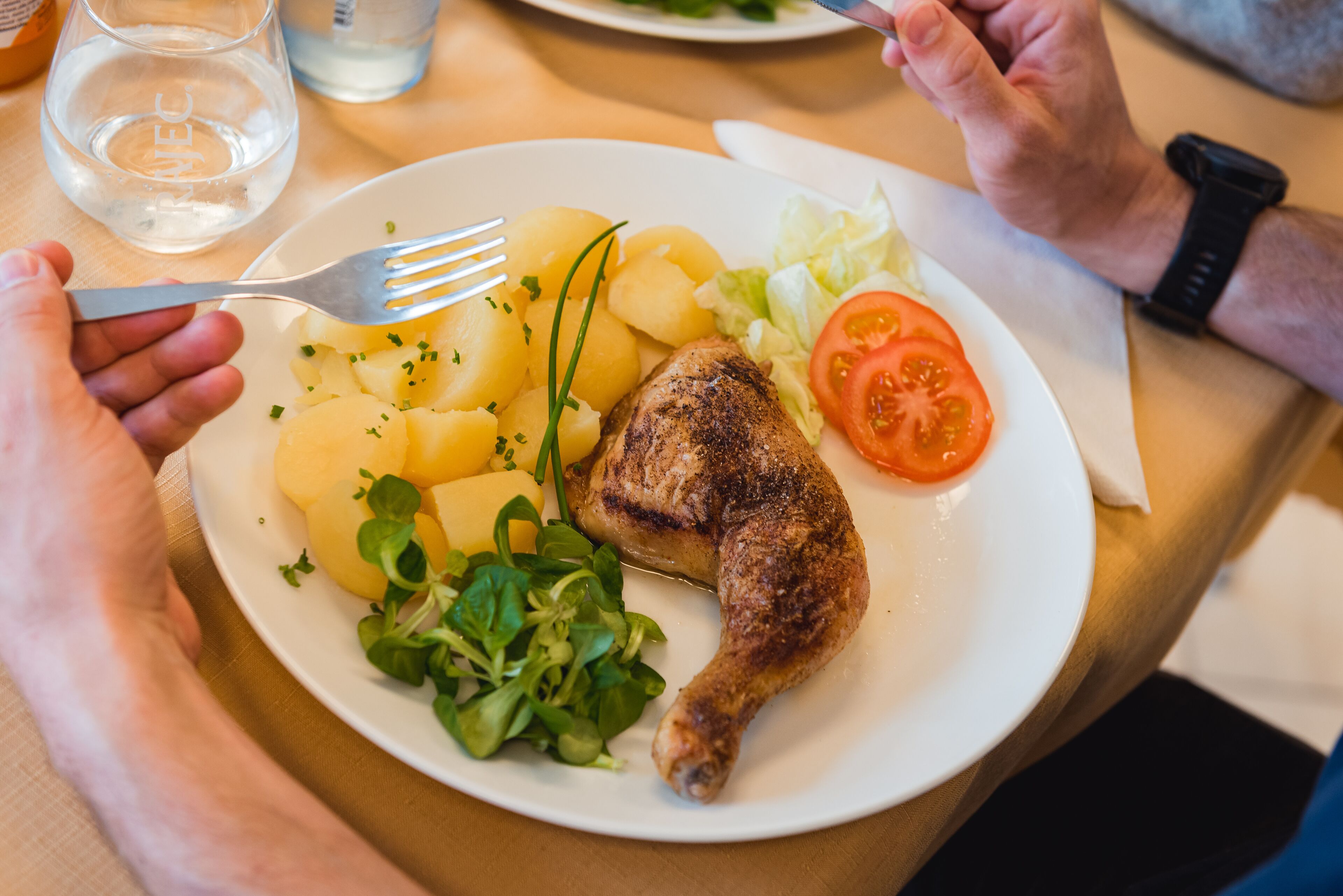 Une assiette contenant un morceau de poulet grillé, des pommes de terre bouillies, une tranche de tomate et quelques légumes verts.