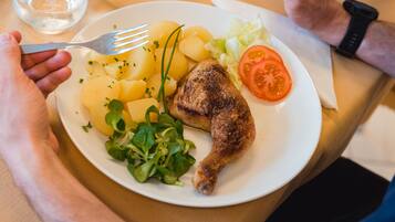 Une assiette contenant un morceau de poulet grillé, des pommes de terre bouillies, une tranche de tomate et quelques légumes verts.