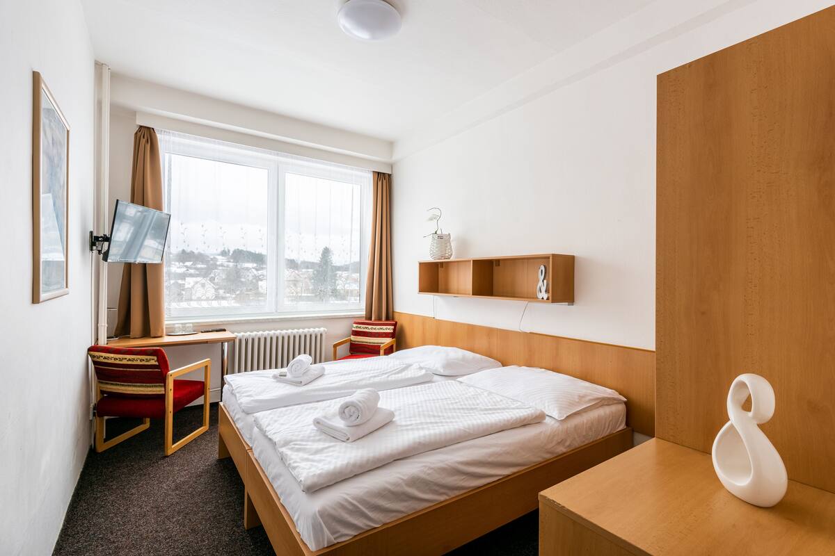 A hotel room with two beds, a desk, a chair, a TV, a window with a view, and a wooden headboard.