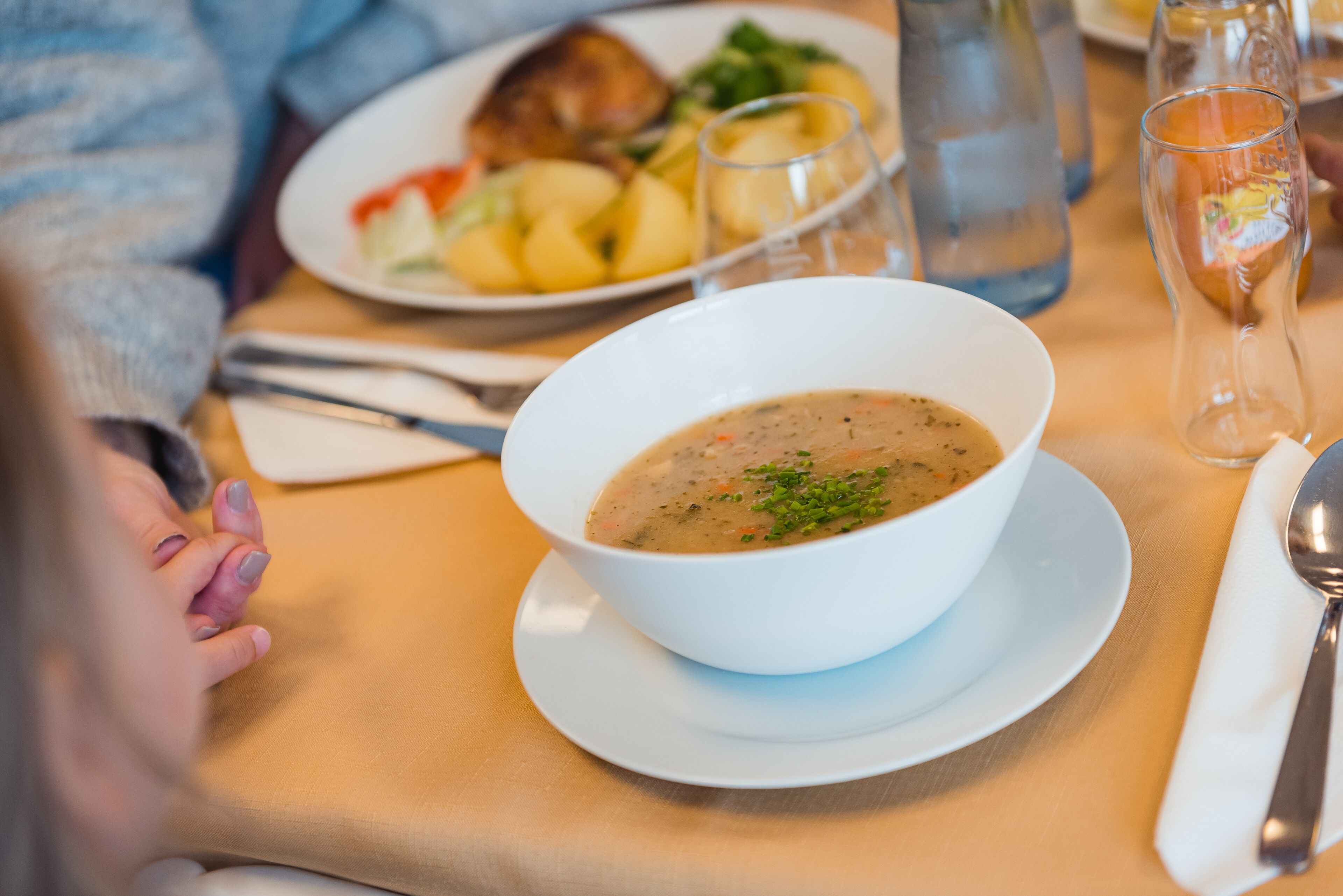A dining table with a bowl of soup, a plate of food, a water bottle, and a glass.