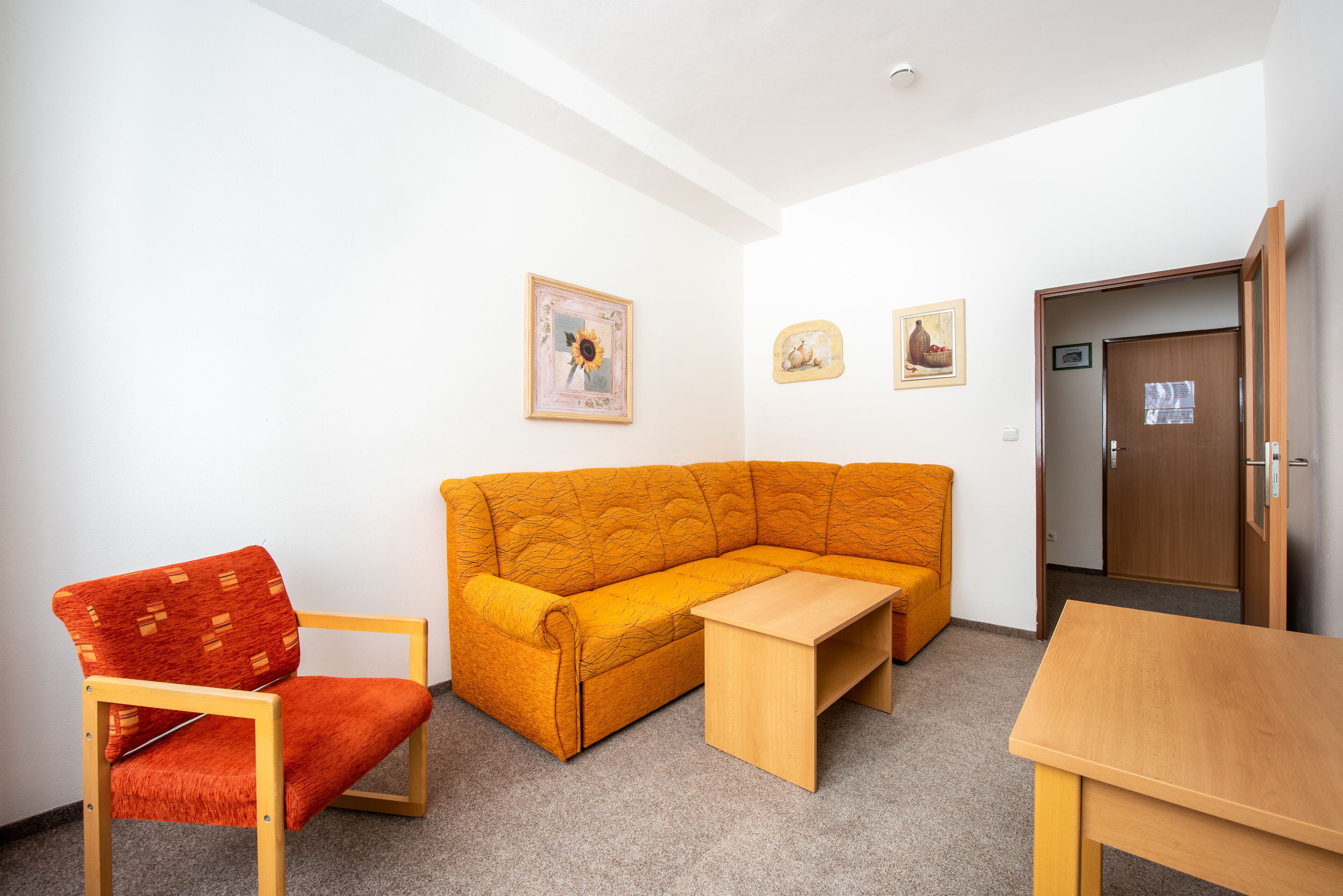 A room with a wooden sofa, a wooden table, and a red chair. There are two framed pictures on the wall.