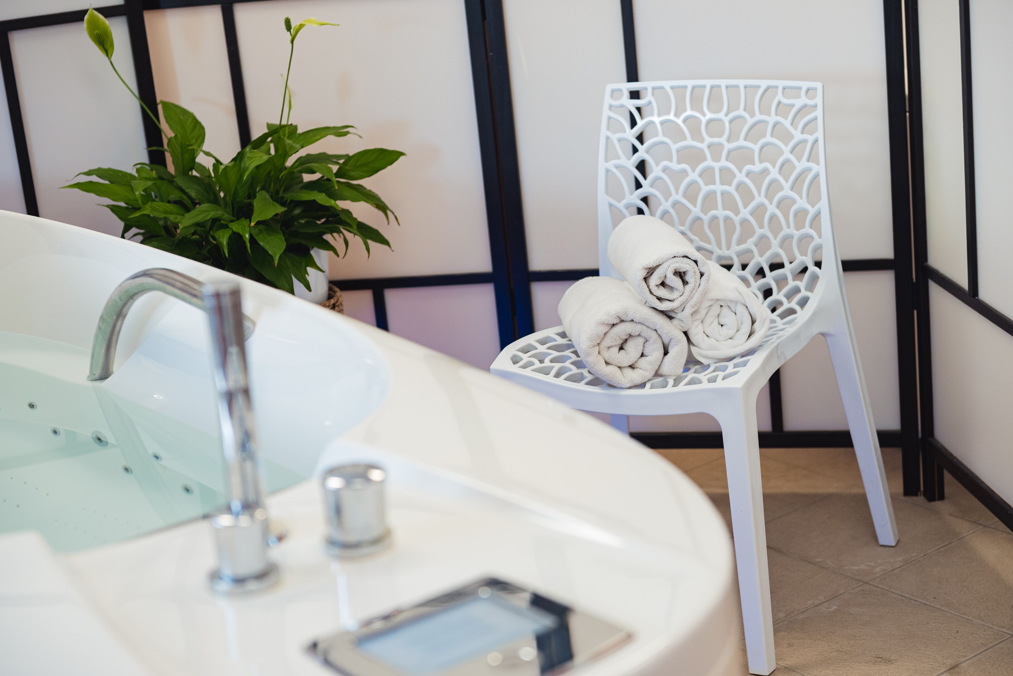 A bathroom with a white sink, a modern faucet, a white chair with rolled towels, and a potted plant.