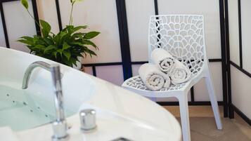 A bathroom with a white sink, a modern faucet, a white chair with rolled towels, and a potted plant.
