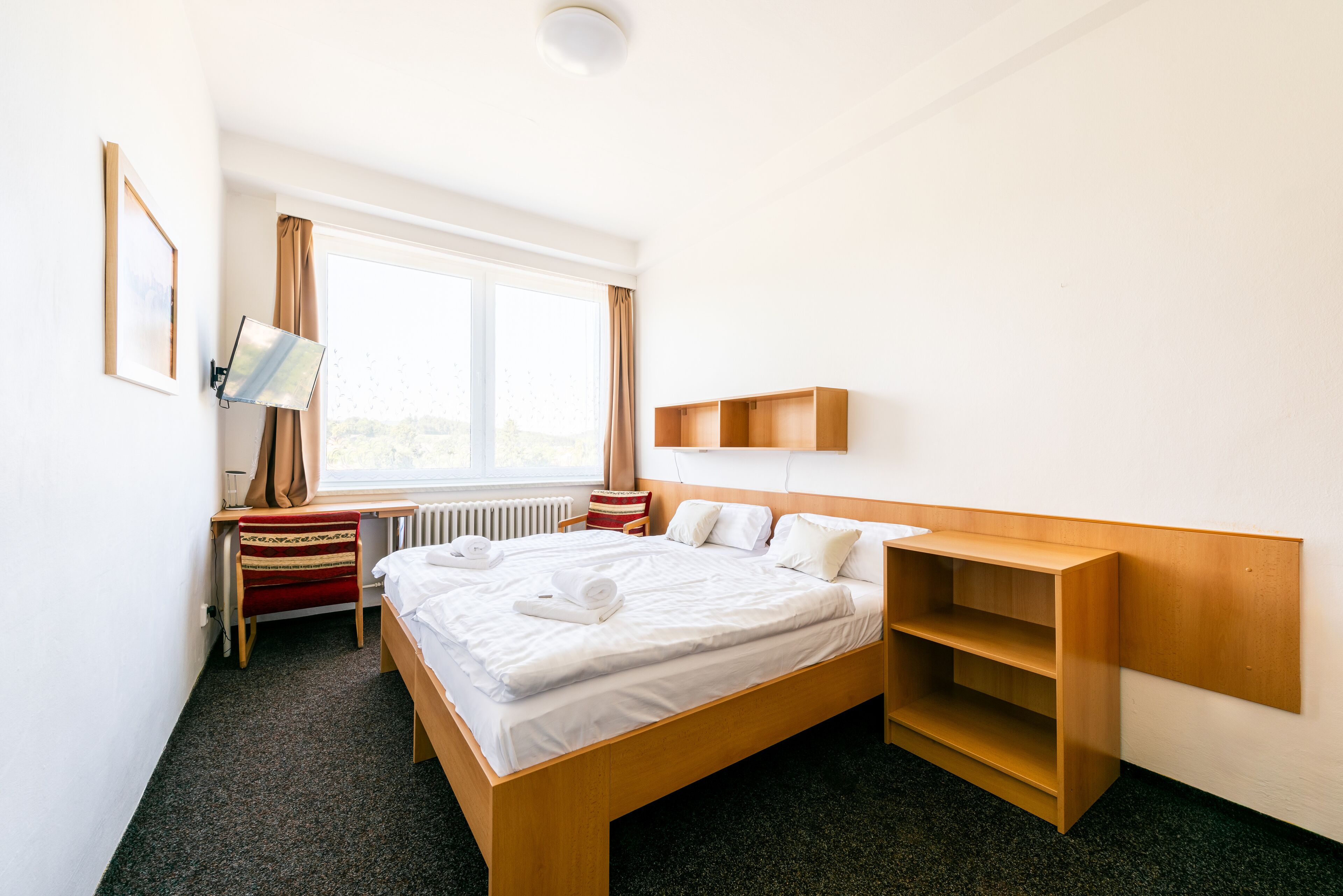 Habitación de hotel con una cama grande, un escritorio con silla, una ventana con cortinas y un estante de madera.