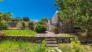 Un bâtiment en pierre, doté d’un toit en tuiles, entouré d’une végétation luxuriante et d’un mur de pierre.