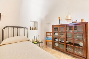 A bedroom with a bed, a wooden cabinet with glass doors, a small table with decorative items, and a chair.