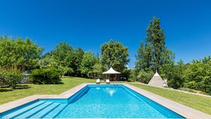 Une piscine rectangulaire, bordée d’une terrasse carrelée, entourée d’une végétation luxuriante et agrémentée d’un belvédère.