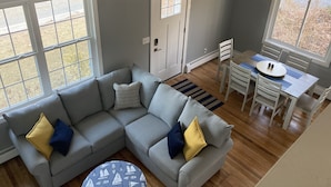 Un salon avec un canapé d’angle gris, une table à manger avec des chaises et un ventilateur de plafond.