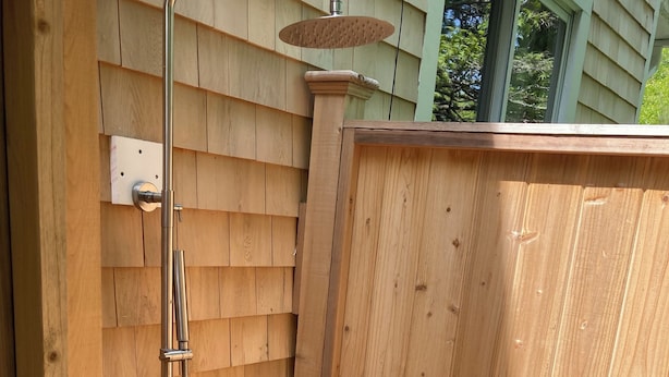 Une cabine de douche en bois, dotée d’un flexible métallique et d’un pommeau de douche à main.
