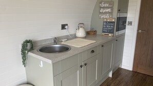 A kitchen with a sink, countertop, cabinets, a kettle, a chalkboard with motivational writing, and a microwave. - Beech Pod Cabin in Beautiful Surroundings Wrexham (Wrexham)