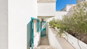A narrow, white-walled corridor with a wooden staircase leading to a balcony.