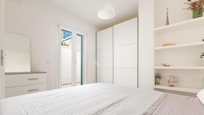 A bedroom with a bed, a wardrobe, a shelf with decorative items, and a door leading to another room.